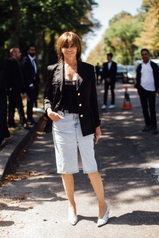 Woman wearing a light wash midi denim skirt, black top, and black blazer