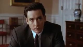 John Cusack looking serious, wearing a suit, in City Hall.