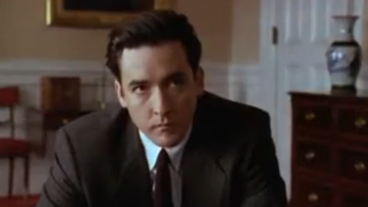 John Cusack looking serious, wearing a suit, in City Hall.