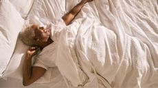 An older woman lying on her back on a new mattress, smiling and stretching in the sun