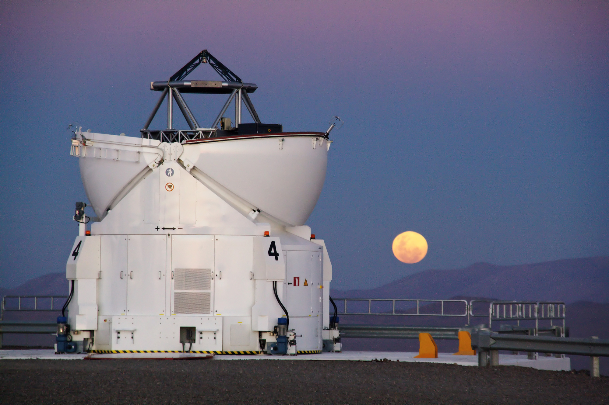 In Chile&#039;s Atacama Desert, home of the Paranal Observatory, the moon rises reddishly with one of the four Auxiliary Telescopes standing in the foreground.