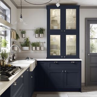 blue kitchen with glass pendant over the sink, herbs hanging on wall, light wood flooring, glass fronted cabinet