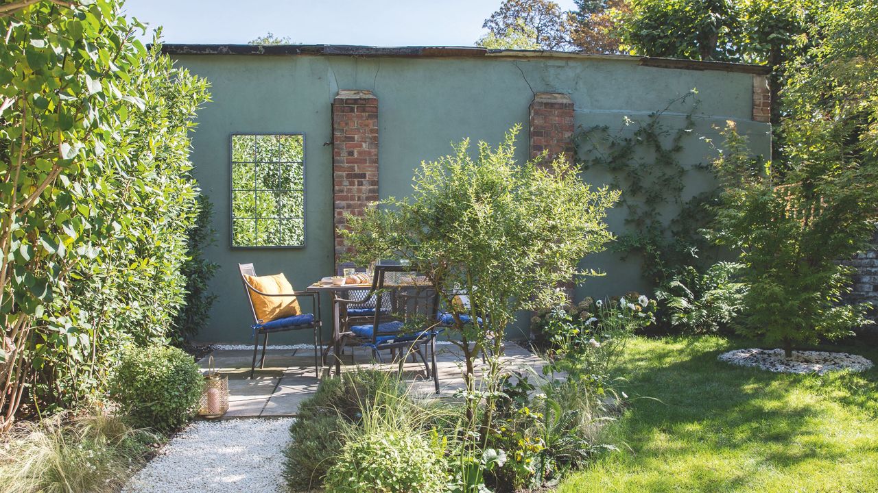 Gravel path through the garden leading to a seating area with table and chairs beside a green wall. Garden redesign of a small city garden in London, owned by Rosie Money-Coutts