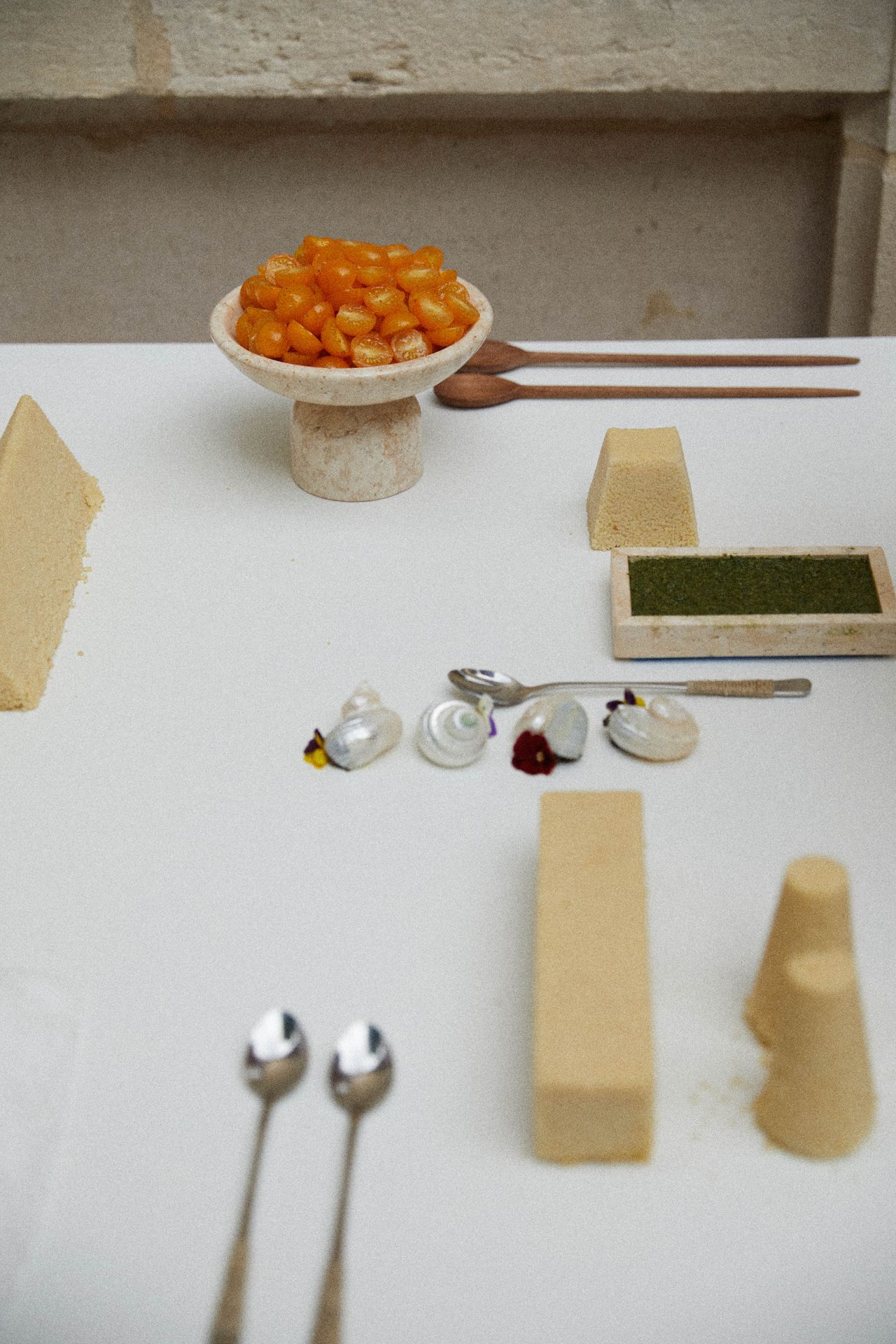 A series of couscous food sculptures, snails, shells, and tomatoes is beautifully positioned on a white cloth table along with silver and wooden cutlery.