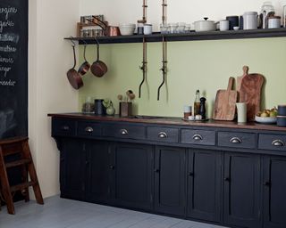 Black kitchen cabinets and coordinating shelf with white wall and green painted backsplash