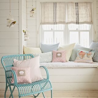 Window seat with blue chair, pink, blue and yellow cushions, and white walls