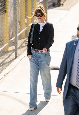 Dakota Johnson leaving Jimmy Kimmel Live! on June 19, 2024 wearing a black cardigan with baggy jeans, a Gucci belt, a Gucci Jackie bag, and white Gucci kitten heels.