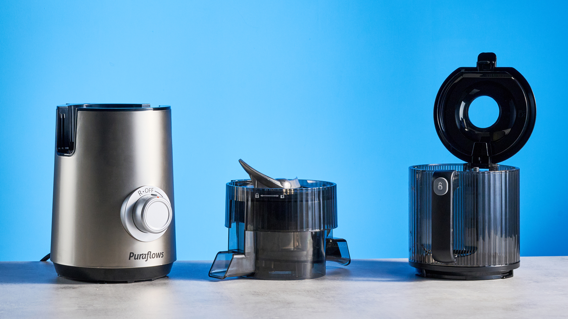 Puraflows Auramist Cold Press Juicer and accessories photographed in front of a blue background