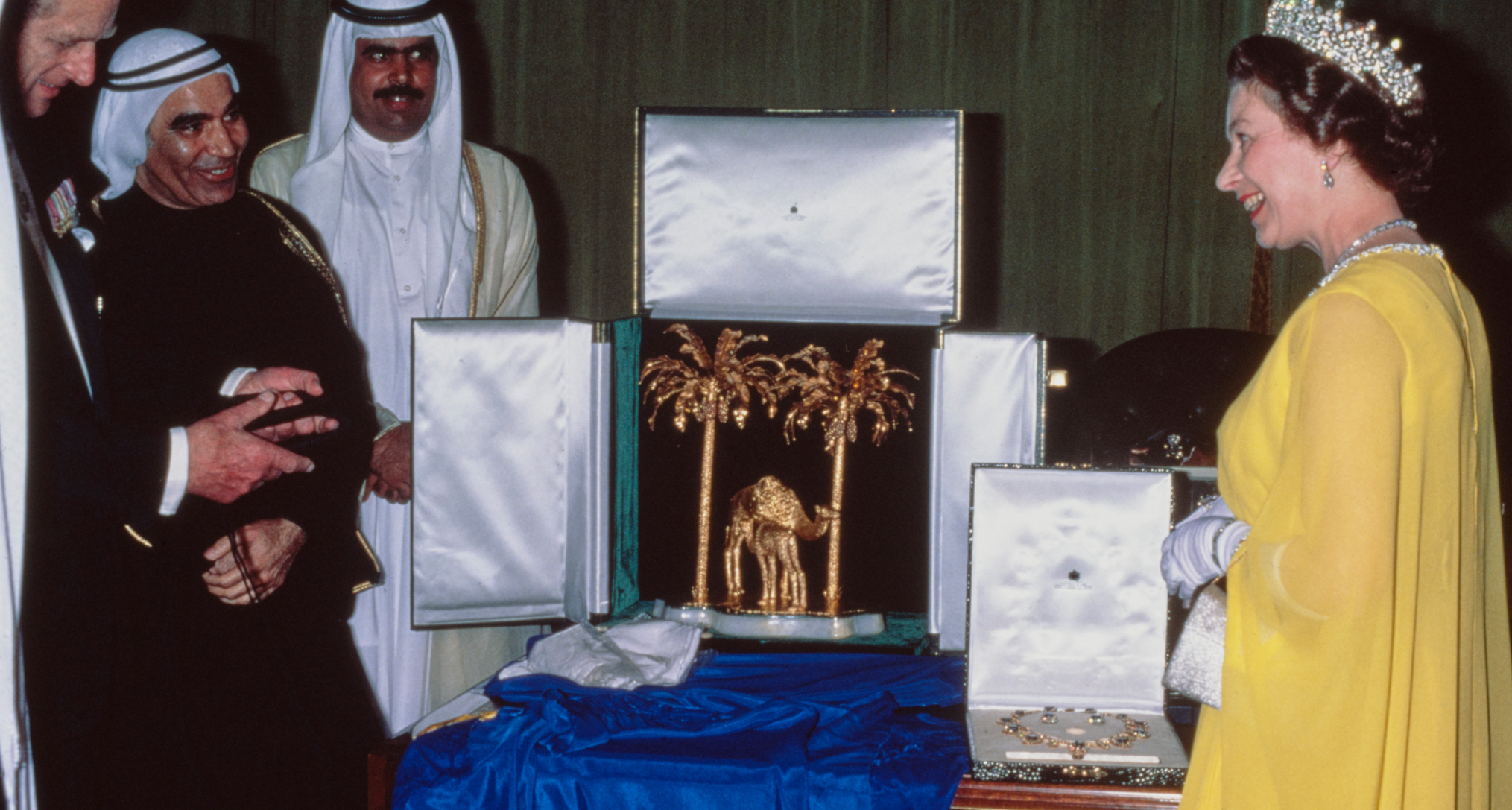 Queen Elizabeth wearing a yellow gown and tiara opening a box of jewelry