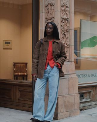 @_livmadeline wears wide leg jeans with a bold red cardigan, and suede jacket.