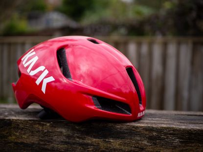 A red Kask Utopia Y aero helmet sits on a wooden bench