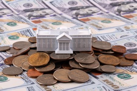 miniature model of the white house sitting on top of a pile of coins and stacks of one-hundred dollar bills