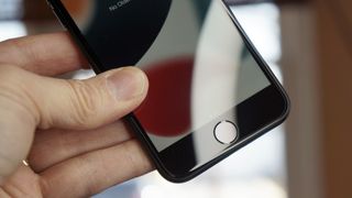 En hånd holder i en mobiltelefon av typen iPhone SE.