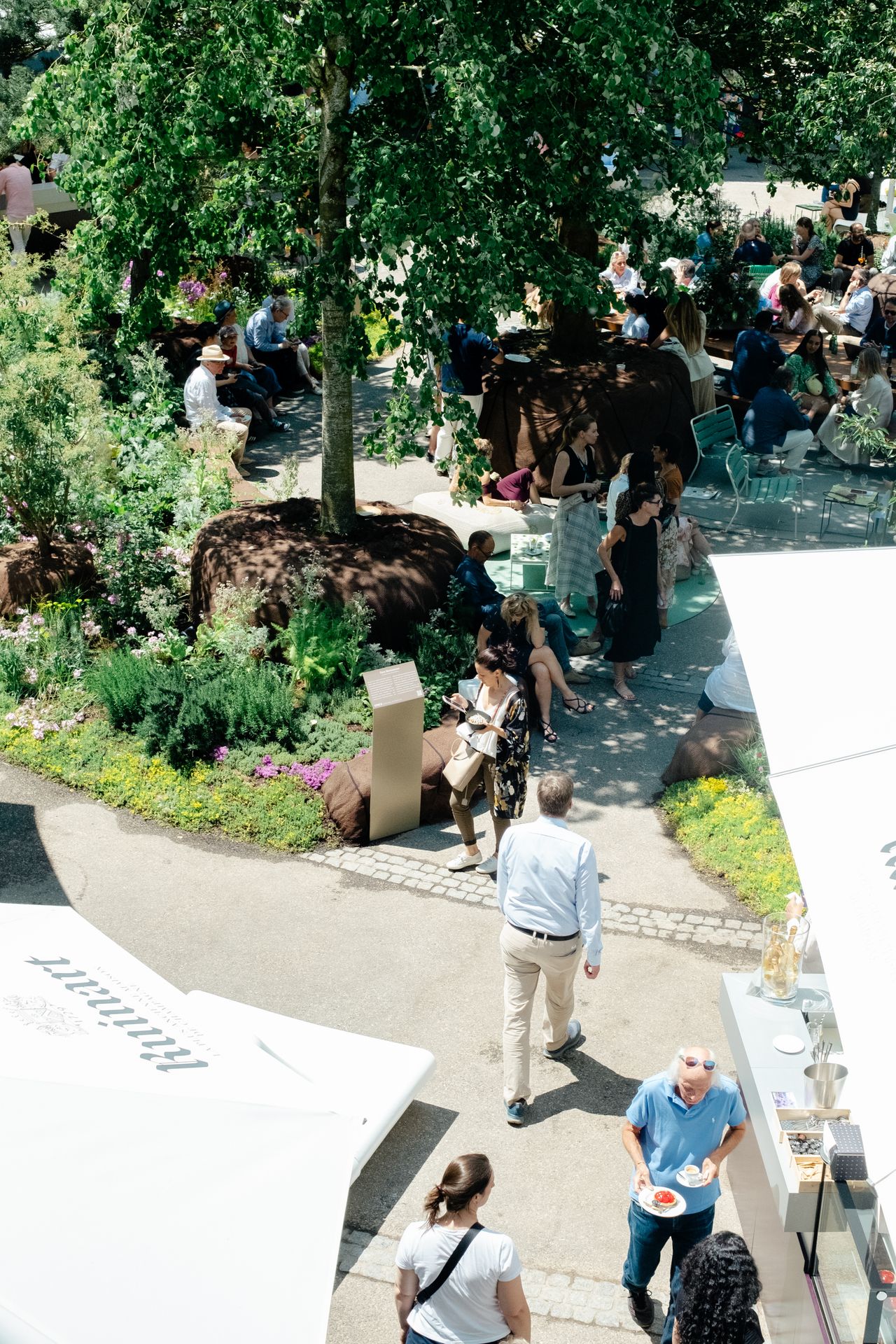 A series of lifestyle images depict people at leisure and play in a Swiss town bathing in sunshine, whether enjoying the weather near the river bank or abstract painting murals at an art fair.