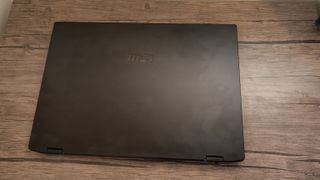 A black MSI Summit E16 Flip Evo laptop sitting on a brown wooden desk