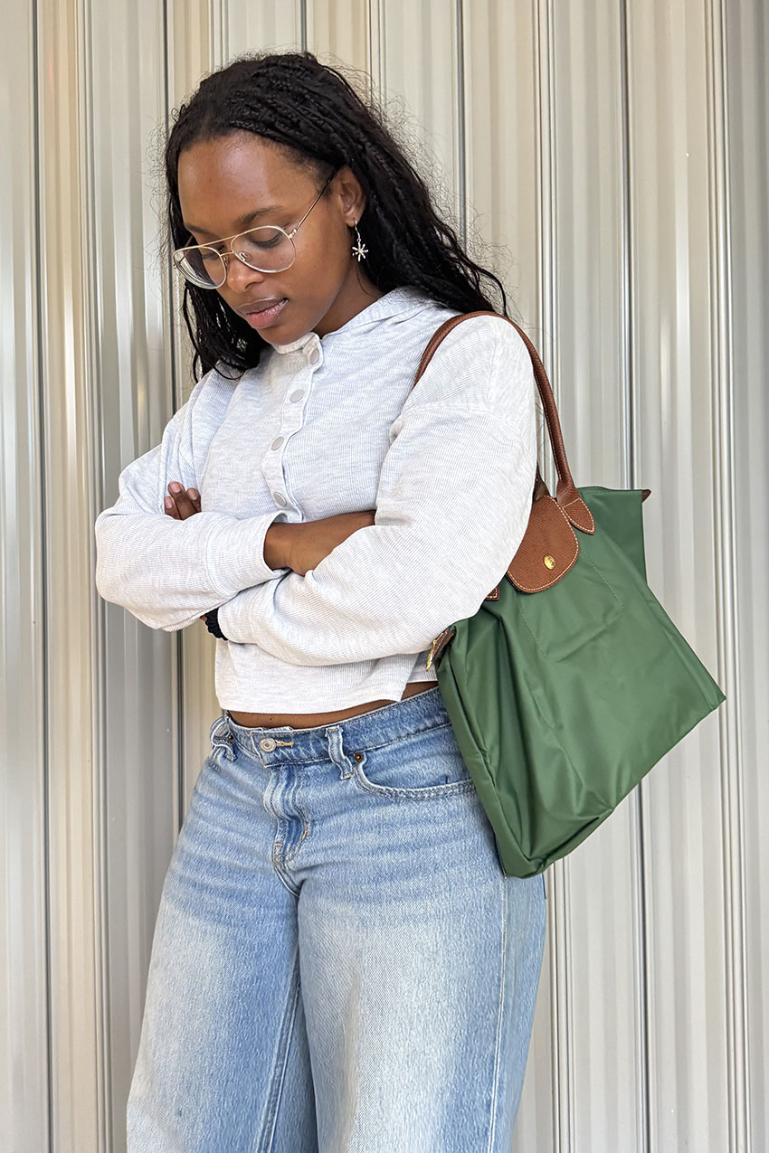 A woman wearing a grey hoodie, blue jeans, and a green canvas tote bag