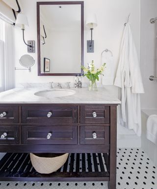 An example of small bathroom storage ideas showing a dark wooden vanity unity with drawers and a marble worktop in front of a mirror