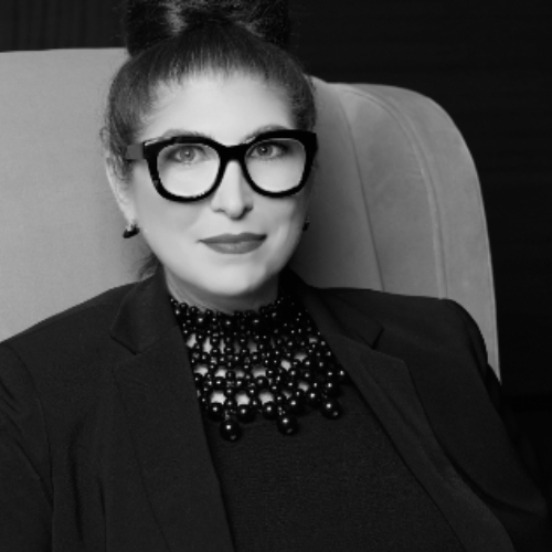 Black-and-white image of a woman in an all-black outfit sitting in a chair