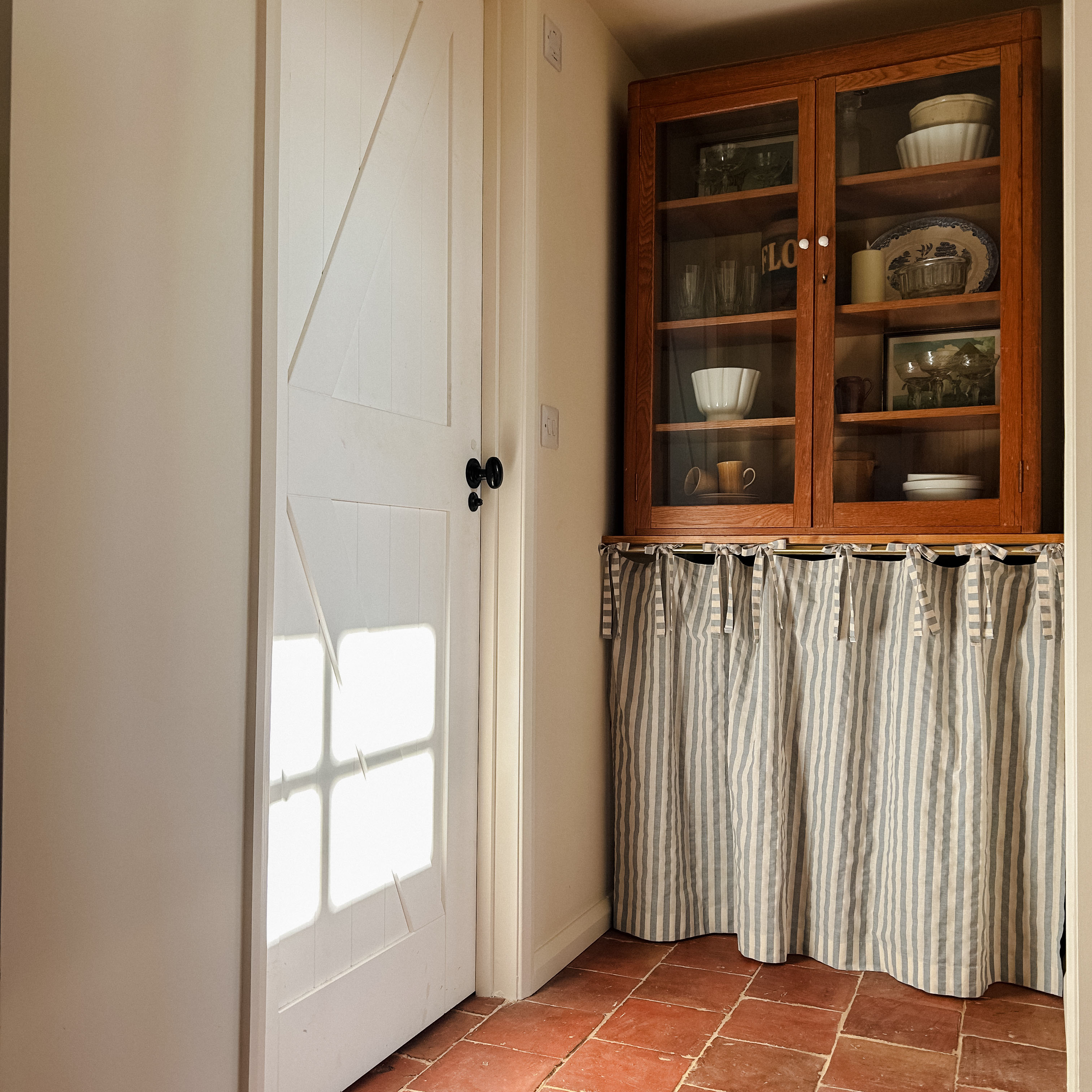 a pantry cupboard with a curtain skirt underneath it