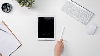 iPad on flat surface and hand reaching for Apple Pencil: best iPad stylus