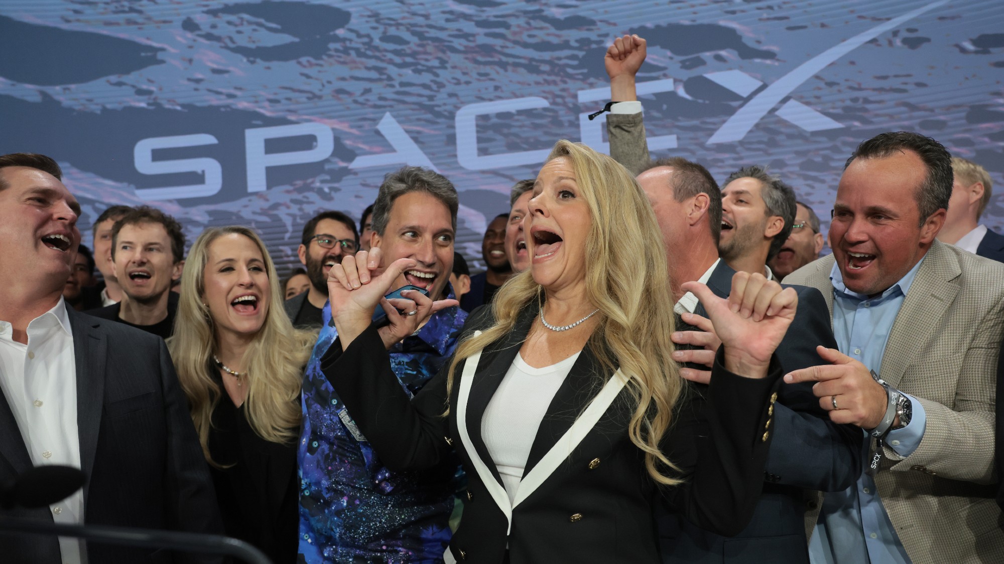 Uma empresária exultante comemora cercada por apoiadores felizes e cercada por banners da SpaceX.