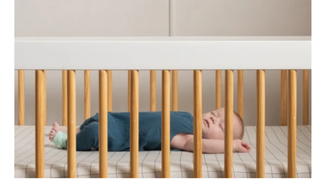 A baby lies sleeping peacefully in a cot, wearing the Owlet Baby Monitor Duo Smart Sock on its foot.