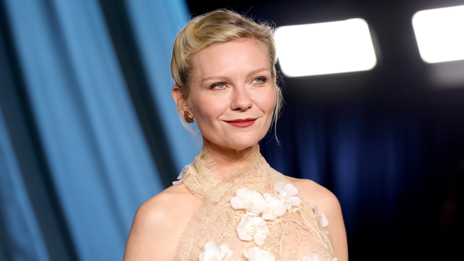 a white woman with blonde hair wearing a floral halter dress and posing in front of a blue background