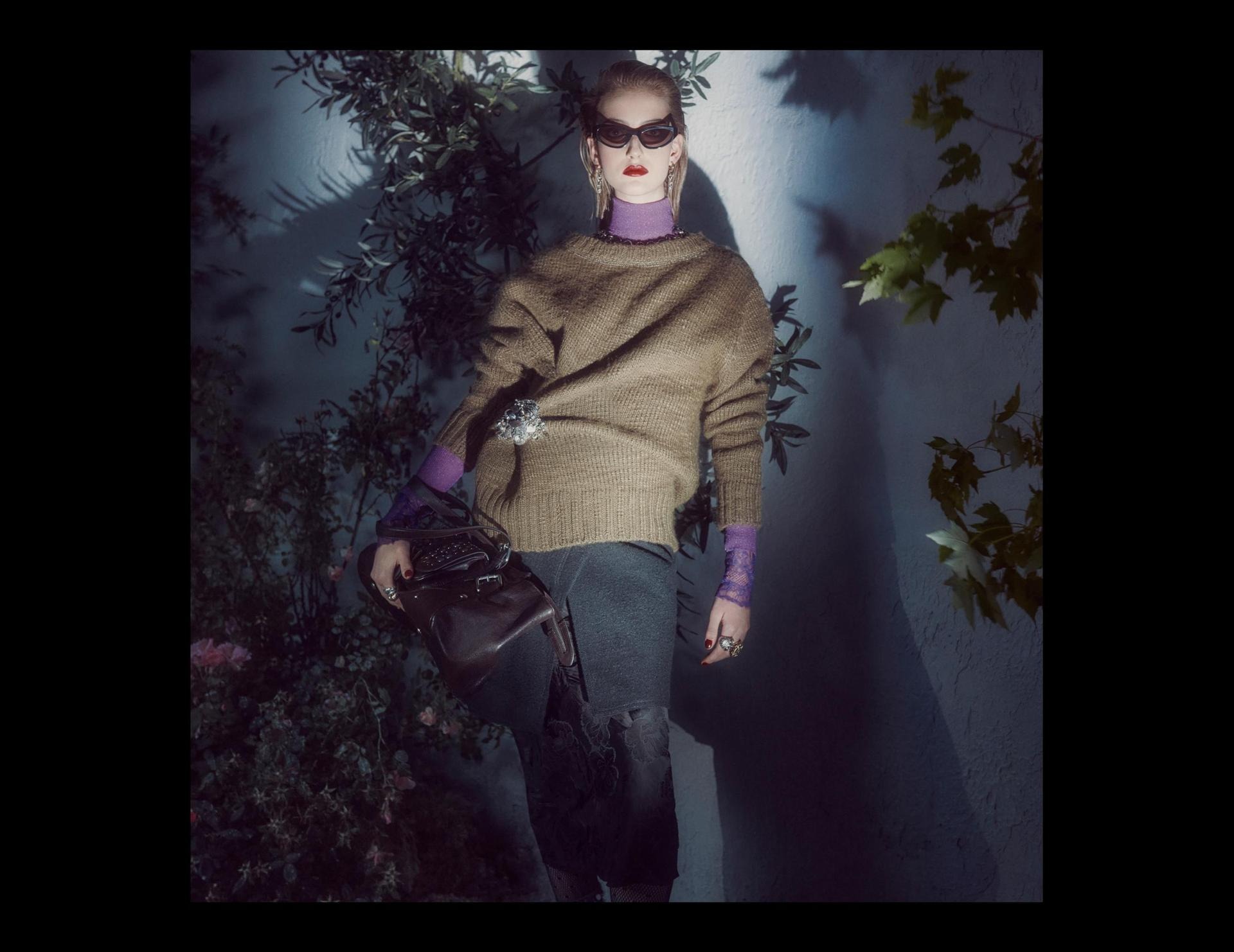 A Zara studio collection model wearing a cinched sweater with a brooch and purple layers