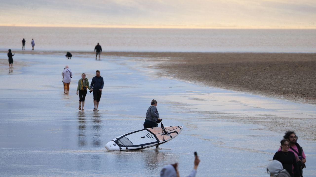 A person drags a paddle board as tourists enjoy the rare opportunity to walk in water as they visit Badwater Basin, the normally driest place in the US