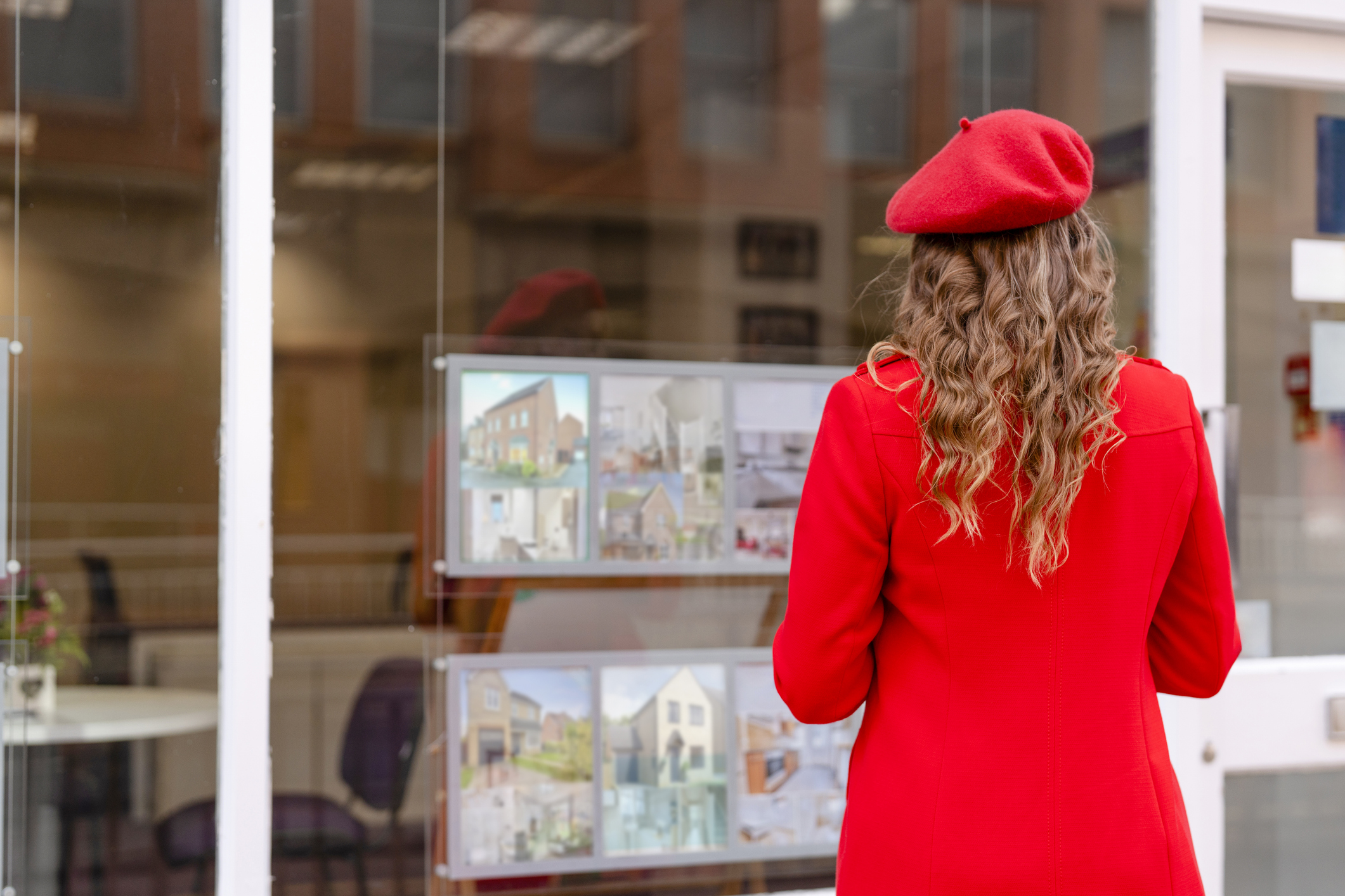 Young woman in red outfit looks at building plans in a display window outside a real estate office