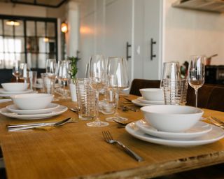 Wooden dining room table set with gleaming glasses and shiny white crockery