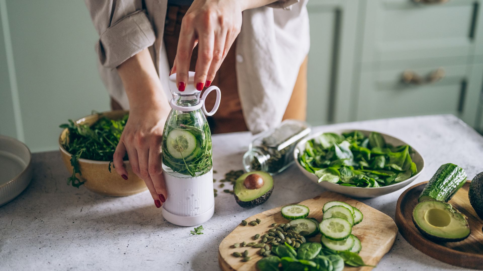 Woman making smoothie with avocado, spinach and other green fruits and vegetables