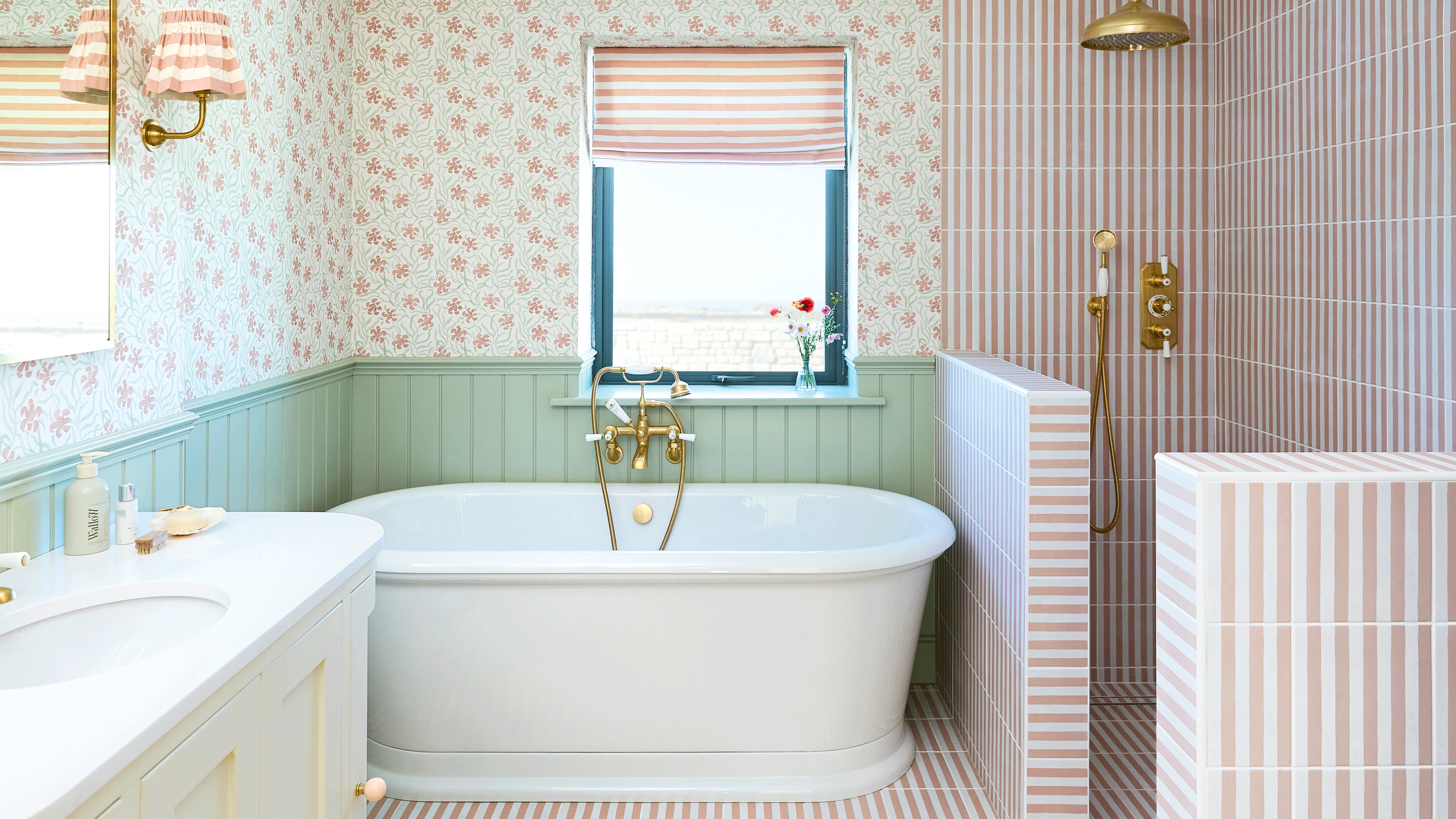 Bathroom with green wall panelling, floral wall paper, pink and white stripe tiles in shower enclosure, stripe wall lights and stripe blinds