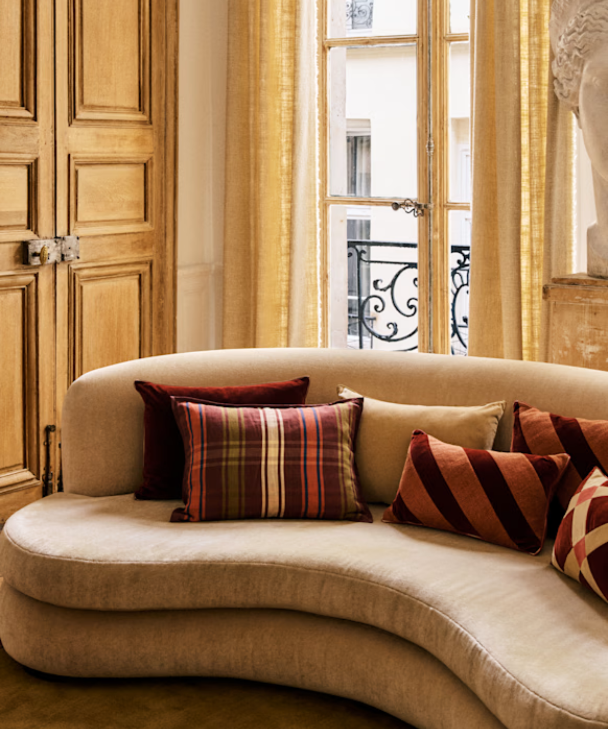 a tan curved couch with several red and pink toned pillows on it