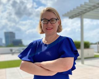 A blonde woman in glasses wearing a blue dress.