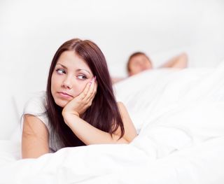 A woman sits in bed, looking worried.