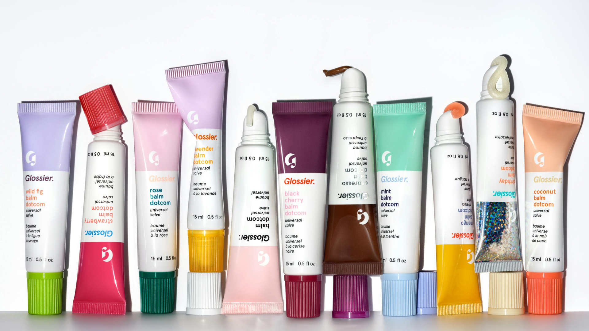 tubes of Glossier balm dot come on light grey background