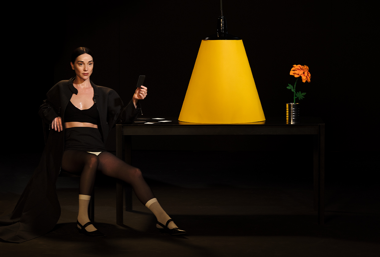 Annie Clark, aka St. Vincent, sitting next to table with large yellow lamp and orange flower.
