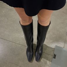 Woman wears black skirt and black knee high boots