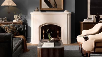 Moody living room styled with a black leather chesterfield sofa, circular armchairs, a fluted marble-top coffee table, and collected objects