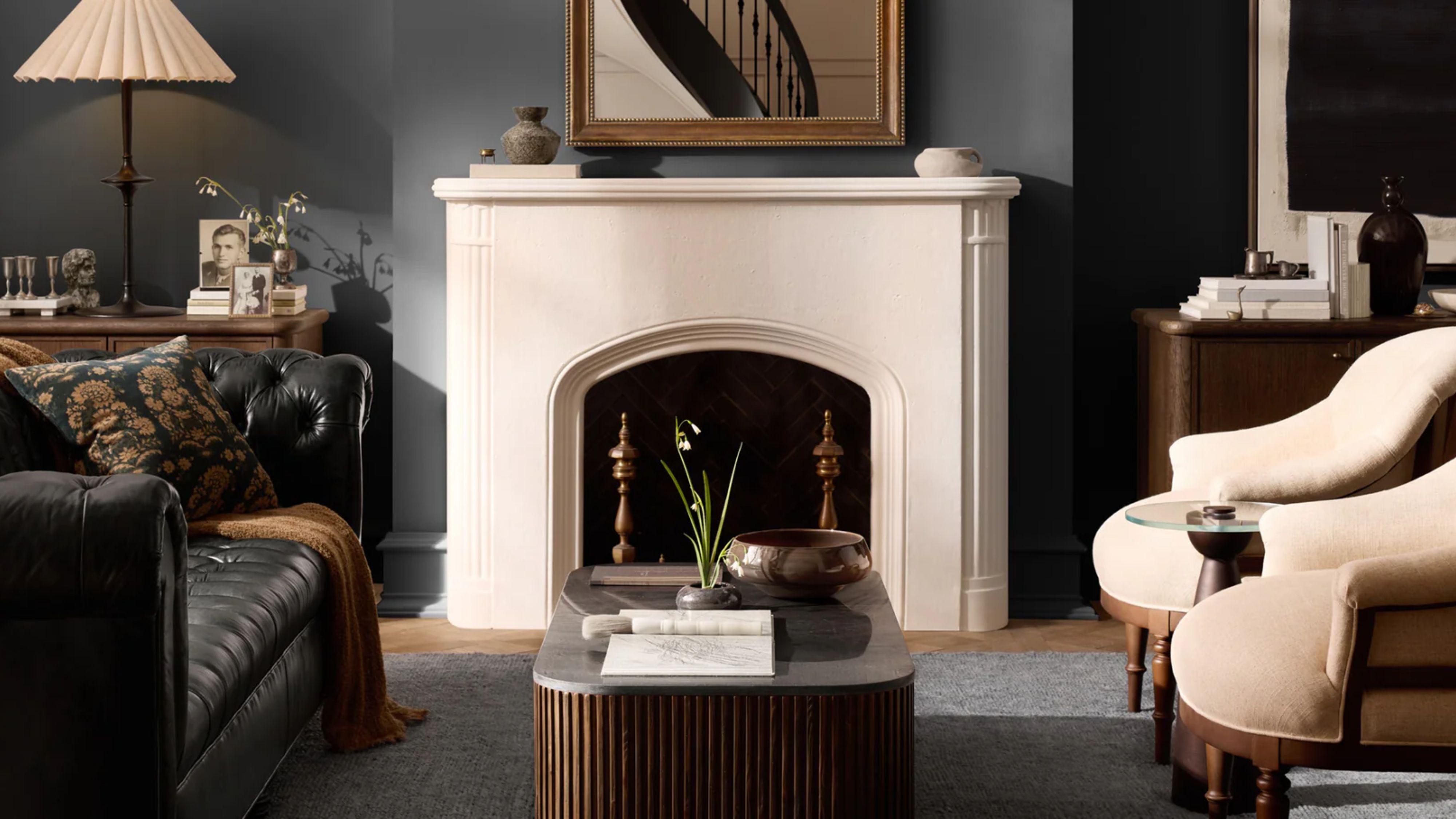 Moody living room styled with a black leather chesterfield sofa, circular armchairs, a fluted marble-top coffee table, and collected objects