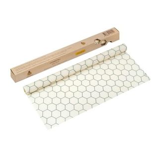 A roll of white beeswax wrap with a black honeycomb pattern on. Next to a light brown cardboard box