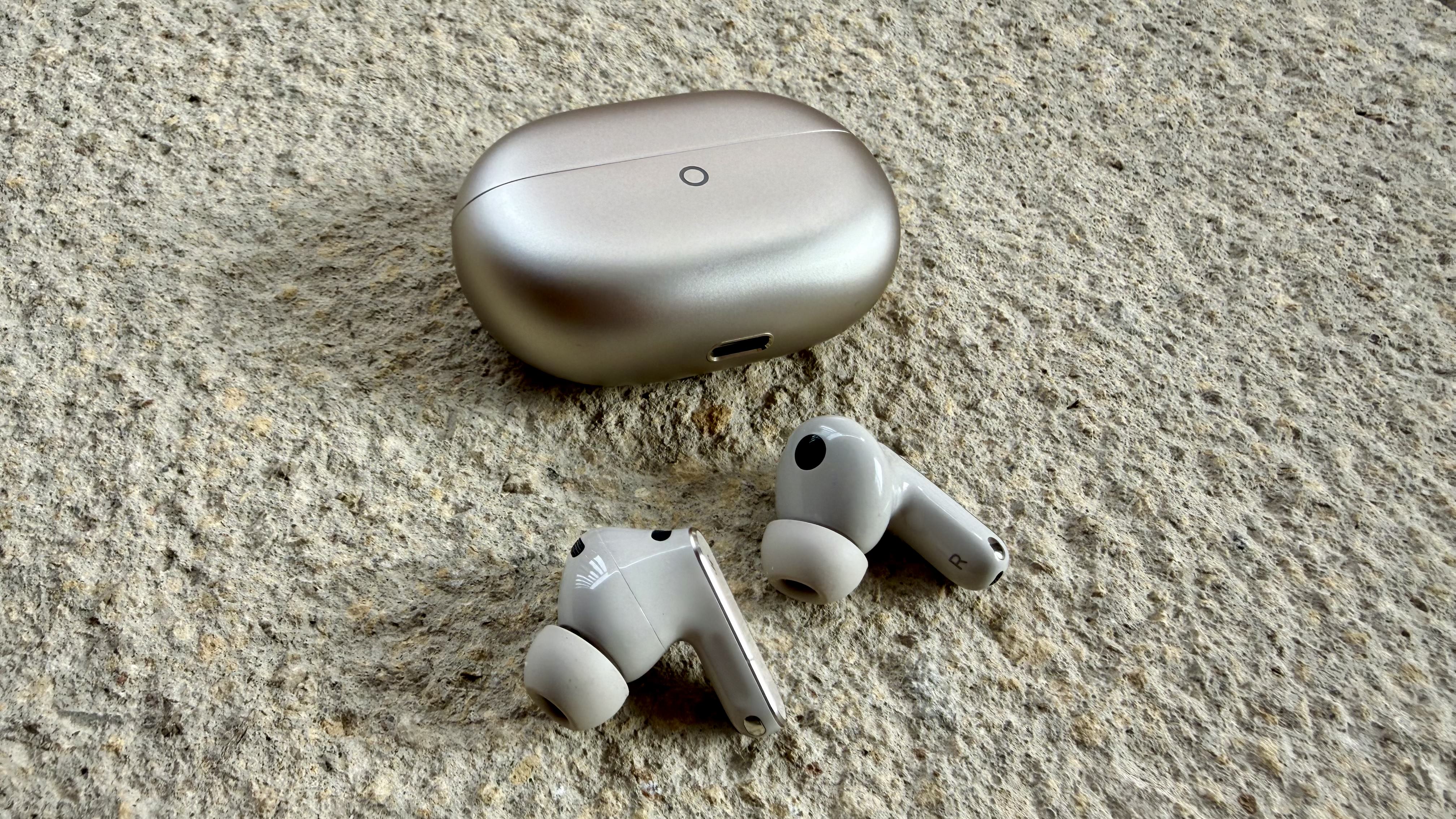 The Huawei FreeBuds Pro 5 buds pictured on a stone surface next to their charging case