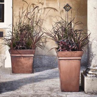 Two metal planters on tiled floor next to cement pillar