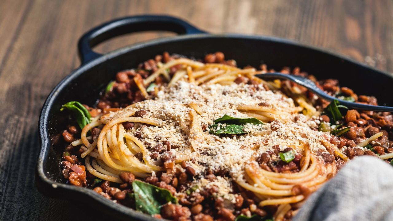 spaghetti bolognese in a cast iron pan topped with fresh basil and grated parmesan