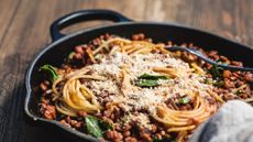spaghetti bolognese in a cast iron pan topped with fresh basil and grated parmesan