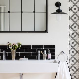 stylish black and white bathroom with black tiled splashback sink wall light and towel