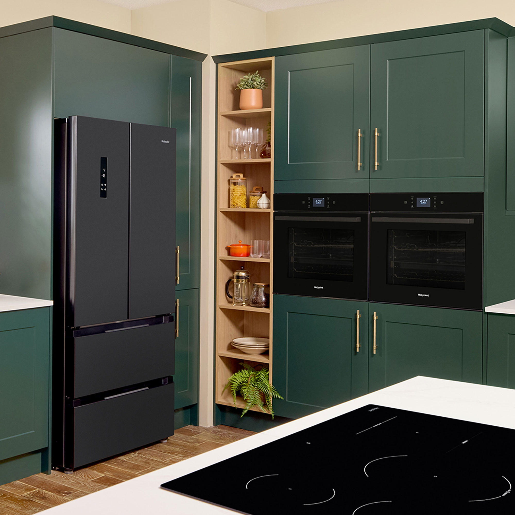Kitchen with green cabinetry, double fridge freezer, hob on island and built-in ovens