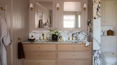 Bathroom with Elephant's Breath by Farrow & Ball painted walls, a double sink vanity unit with marble countertops, wooden drawers, two mirrors and sconces either side.