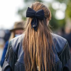 Argan oil for hair: A woman with long brown hair and blonde balayage wearing a black bow in her hair and a black leather jacket